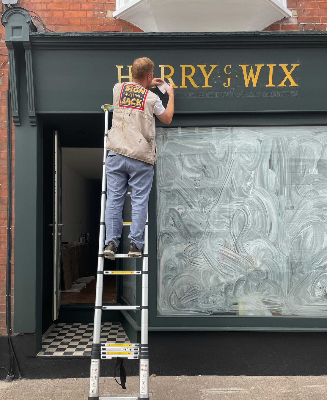 a person standing on a ladder painting a gold sign 