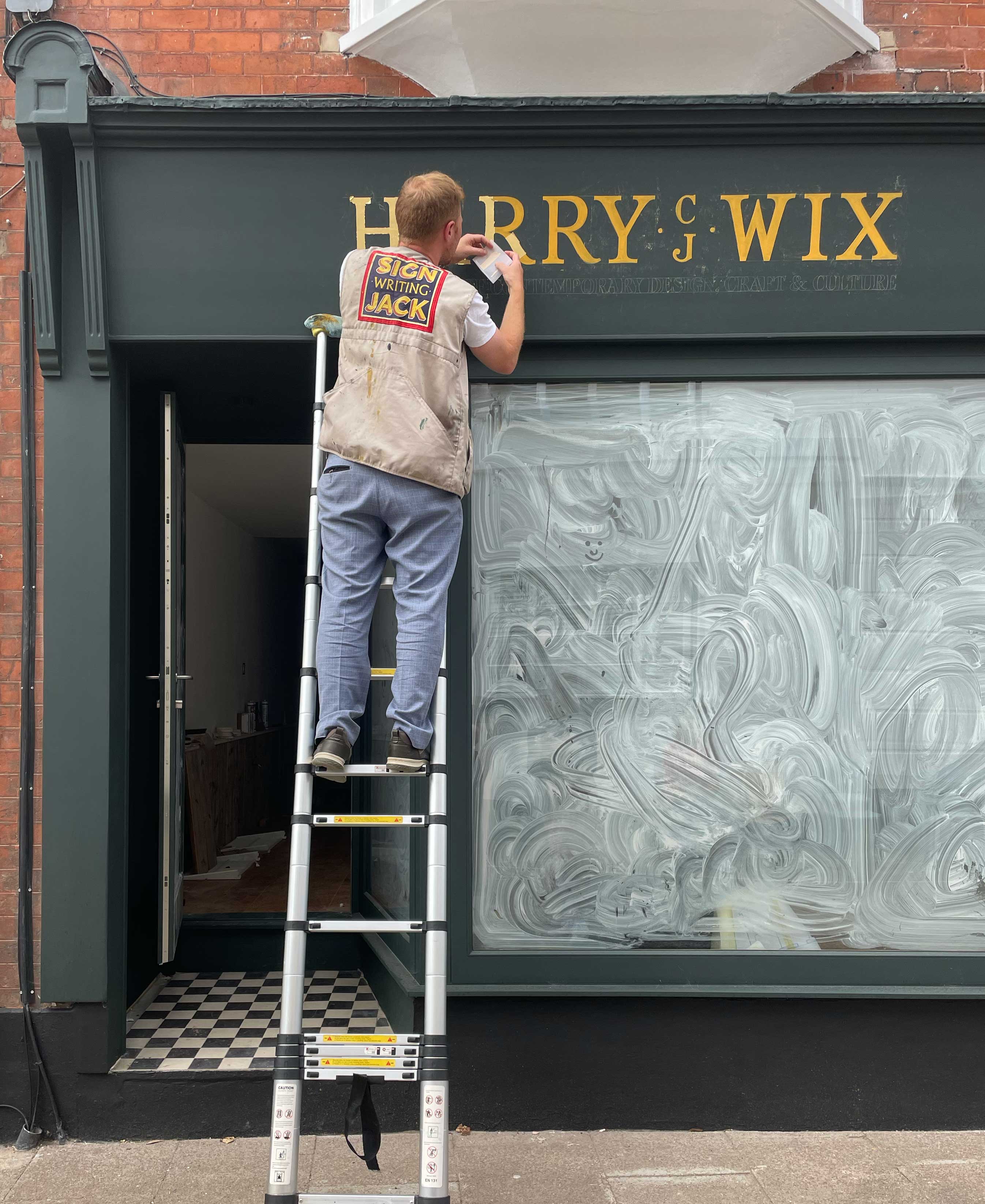 a person standing on a ladder painting a gold sign 